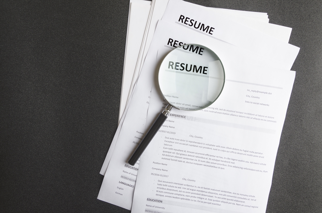 Picture of a stack of resumes with a magnifying glass on top